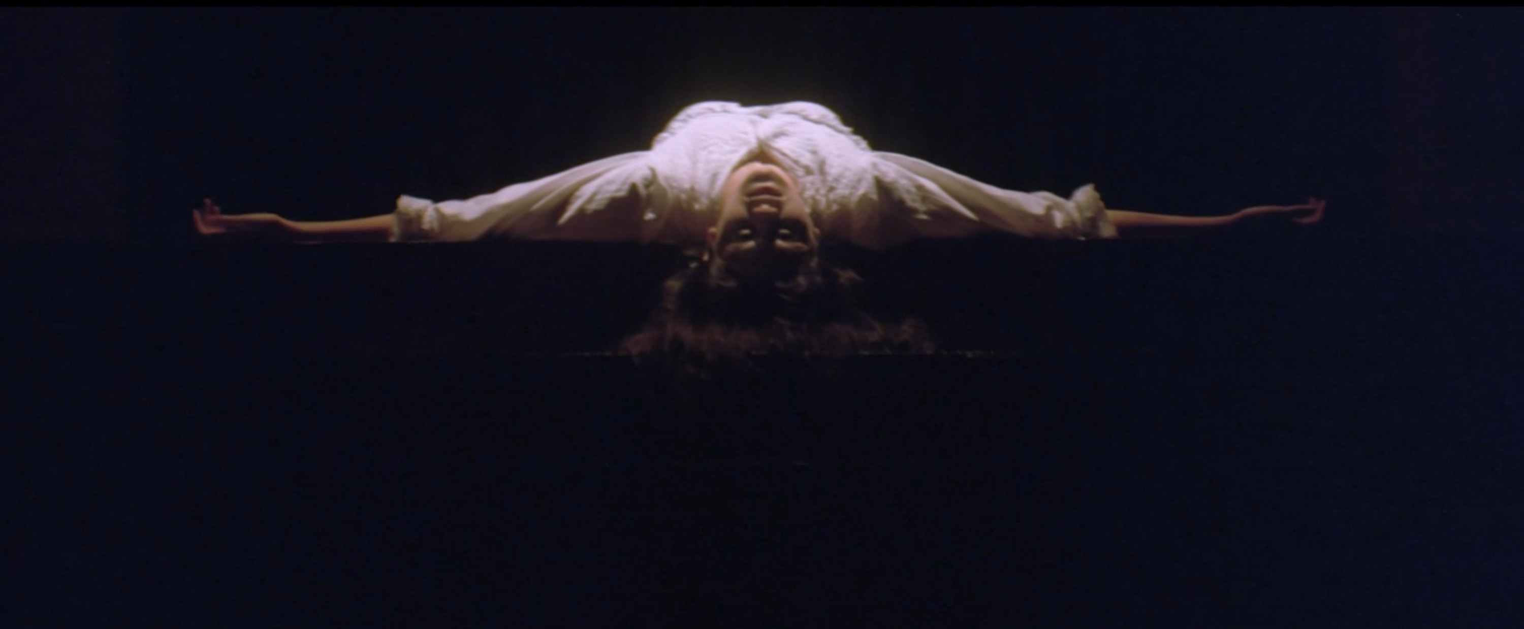 A women laying on her back with her hands spread wide as if she were possessed