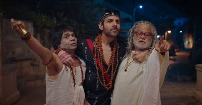 Kartik Aaryan is dressed as a priest and is holding onto Rajpal Yadav and Sanjay Mishra