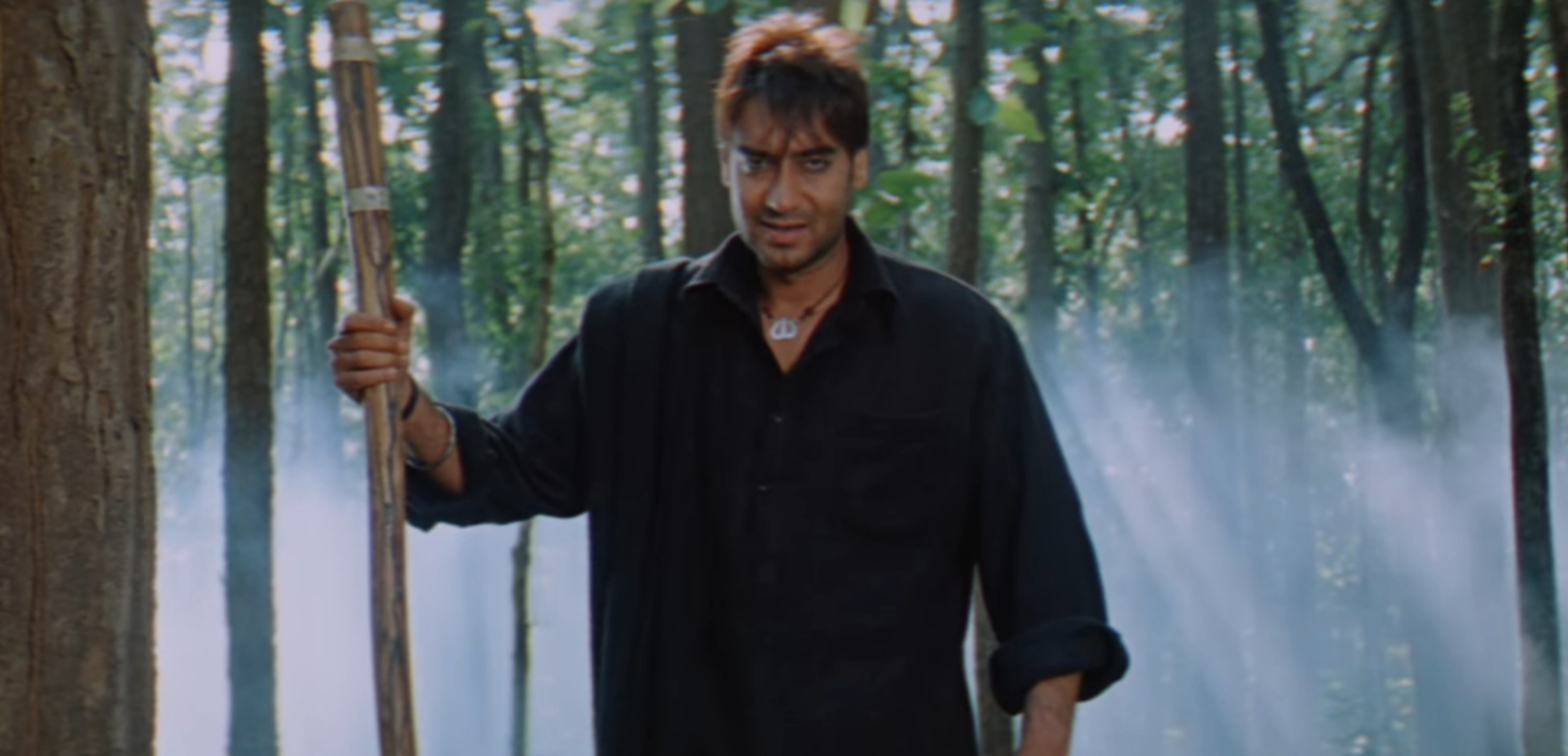 Ajay Devgn standing in the middle of the jungle with a stick