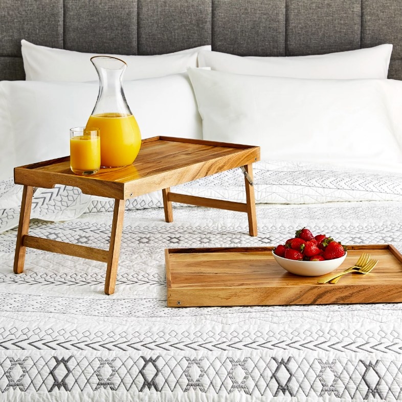 Wood tray with orange juice and bowl of strawberries on a bed