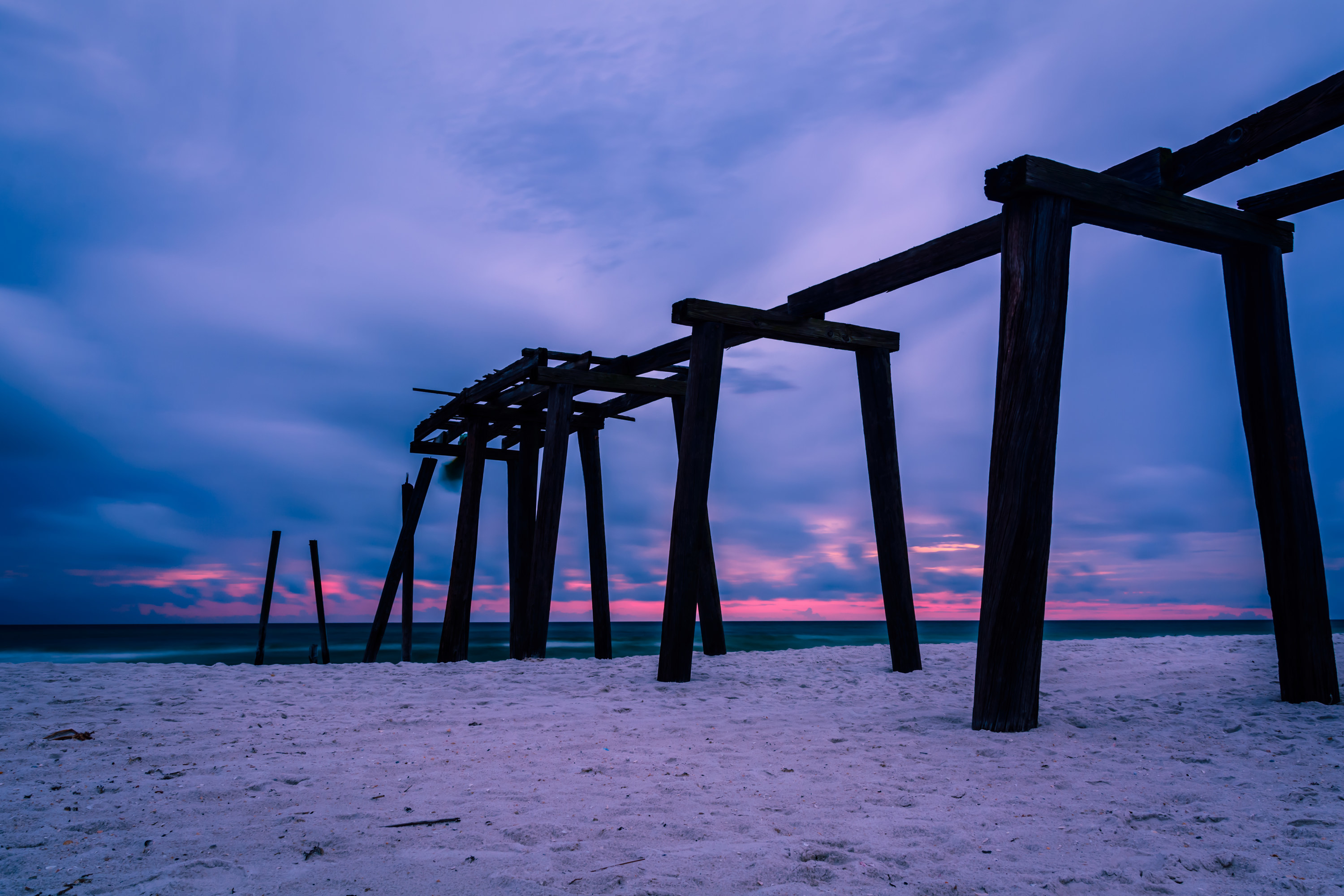 Remains of a pier leading out to the ocean at sunset