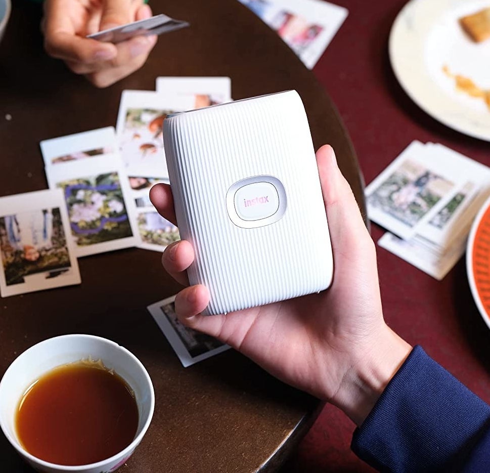 someone holding the printer and polaroids on a table in the background