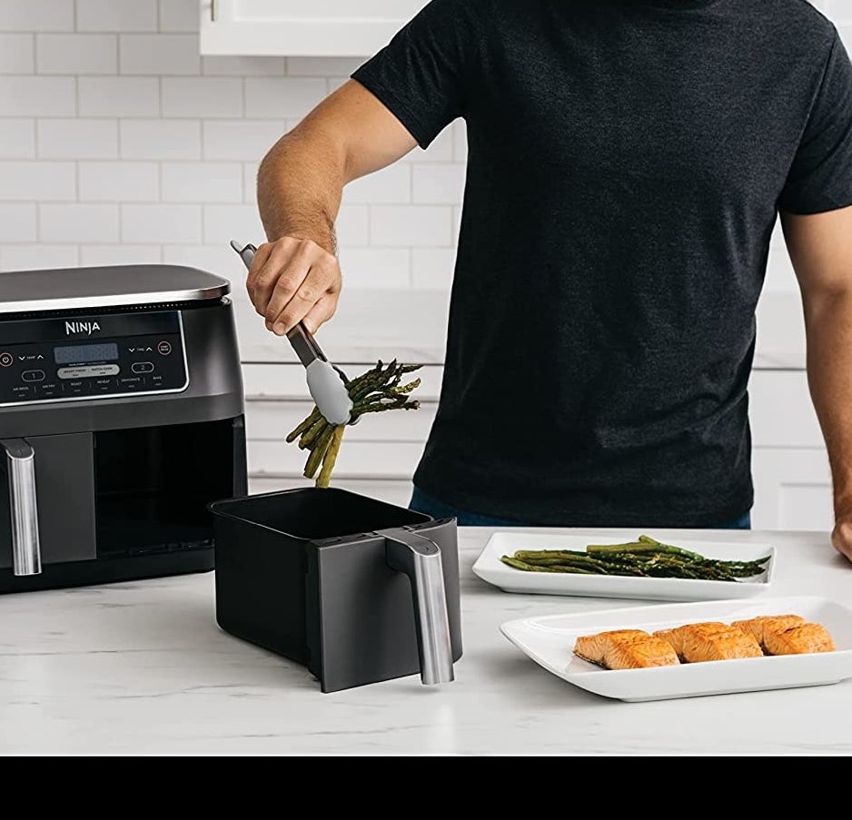 a person putting asparagus into one of the air fryer baskets