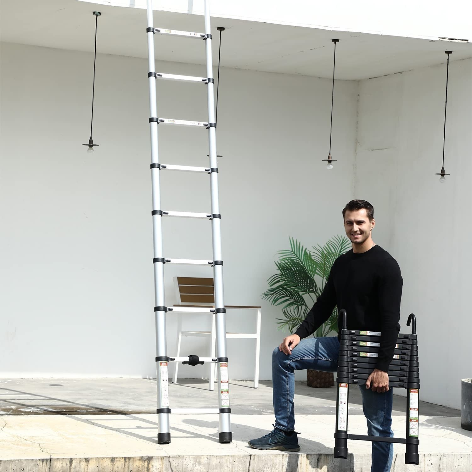 a smiling person standing next to the telescoping ladder while holding up a folded down one in their arms