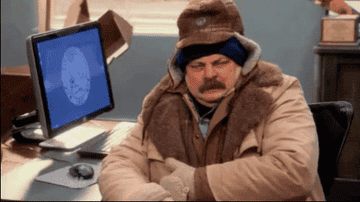 A man wearing winter clothes shivering in an office.