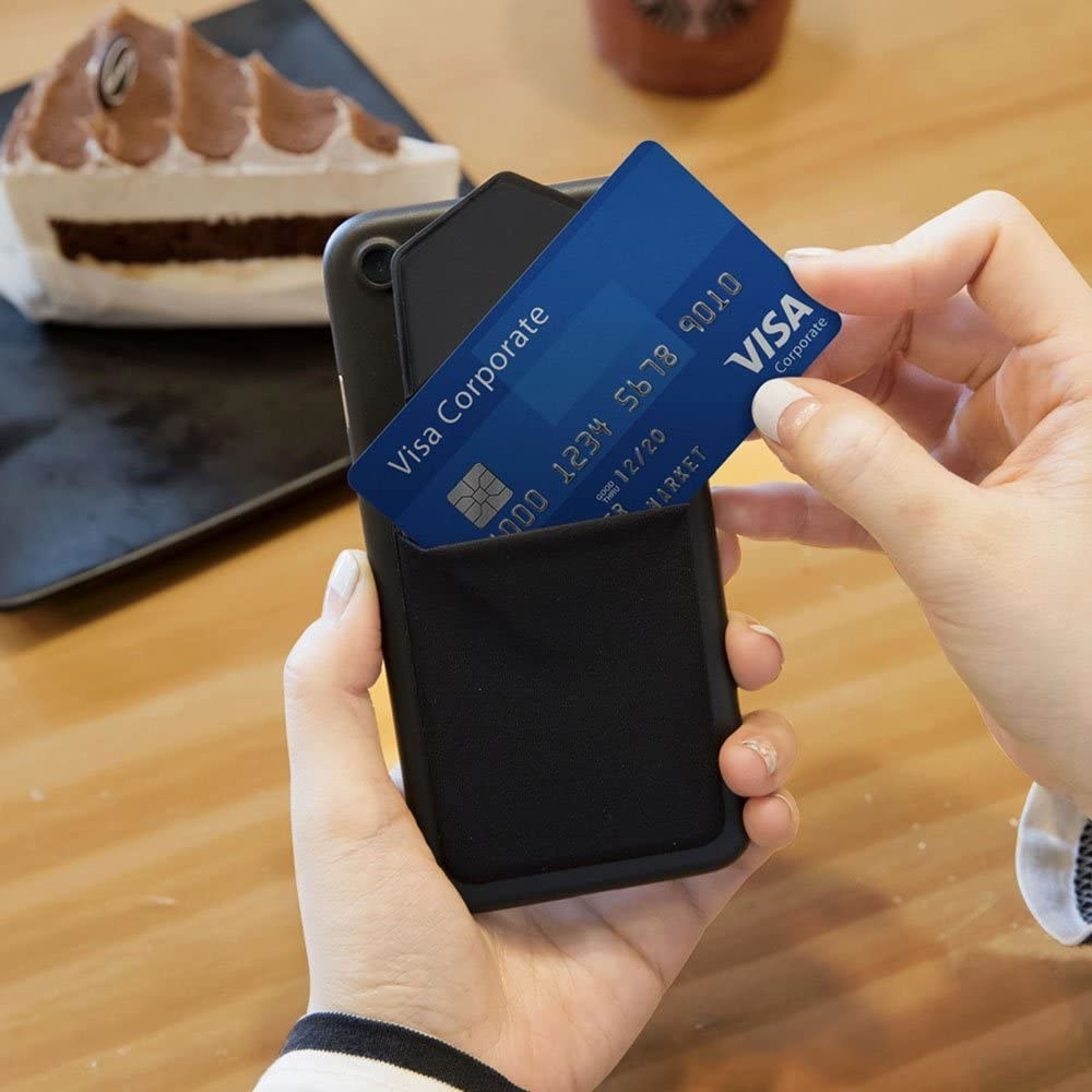 a person holding a phone with the stick-on wallet on the back