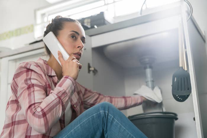 woman on the phone while trying to control the water from a sink pipe