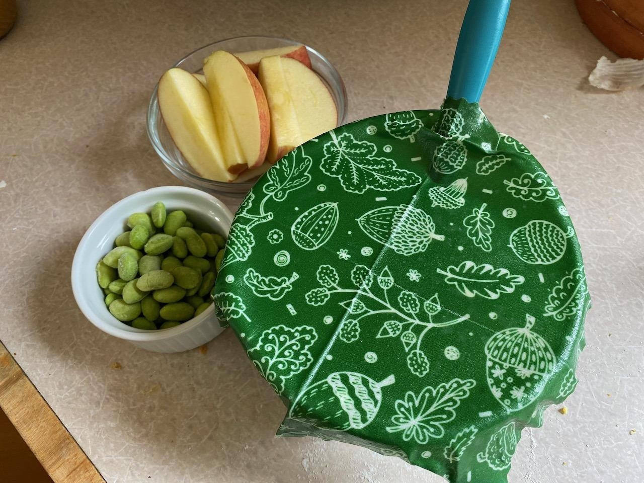 Reviewer image of green patterned beeswax wrap covering a bowl, next to two small bowls