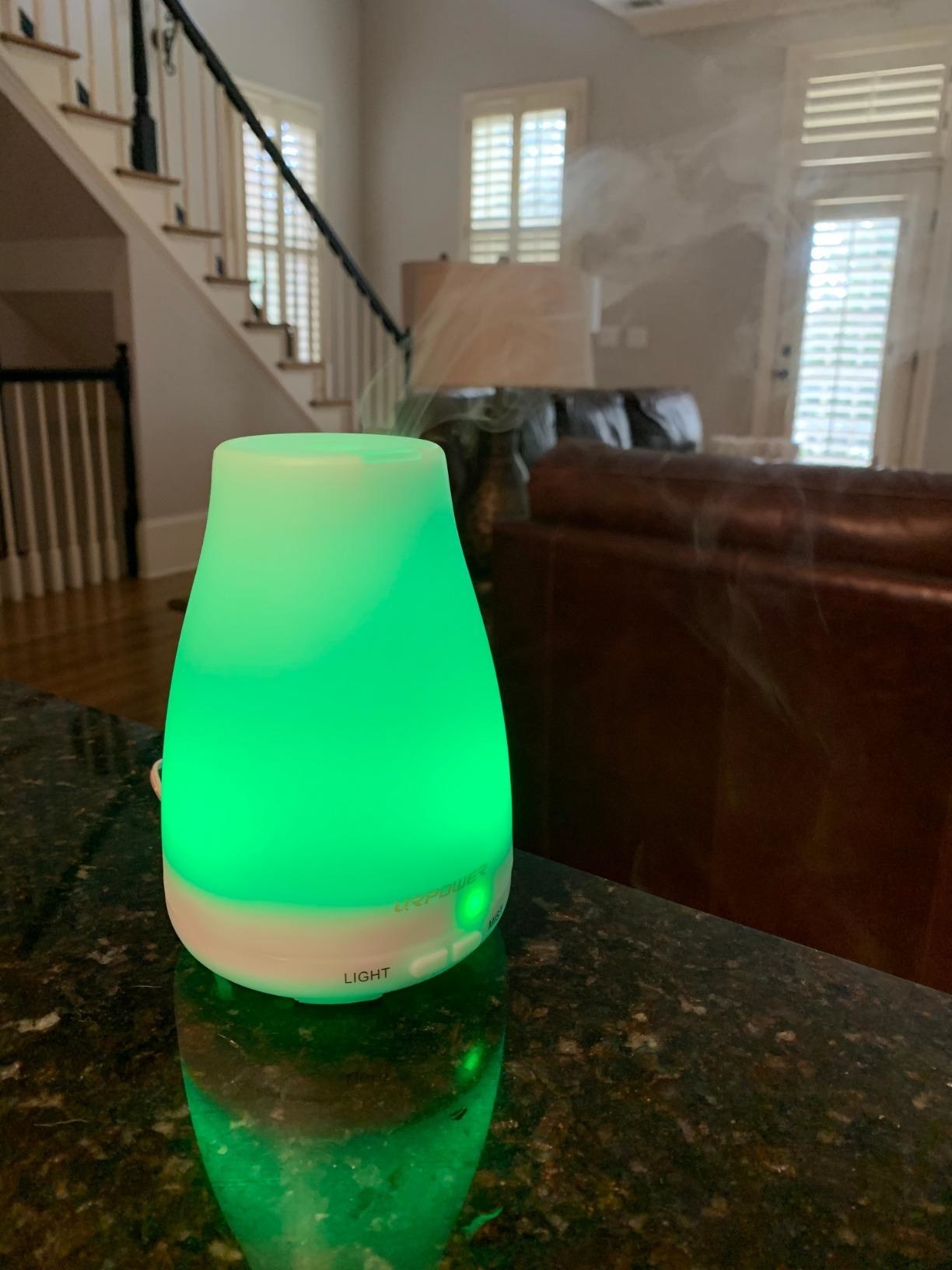 mini essential oil diffuser with green light on top of marble table