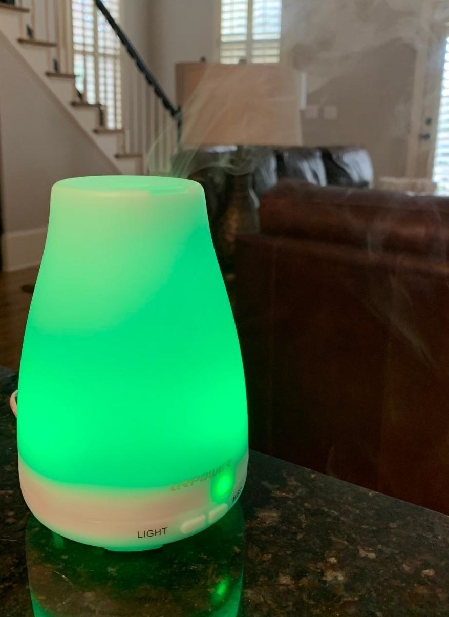 mini essential oil diffuser with green light on top of marble table