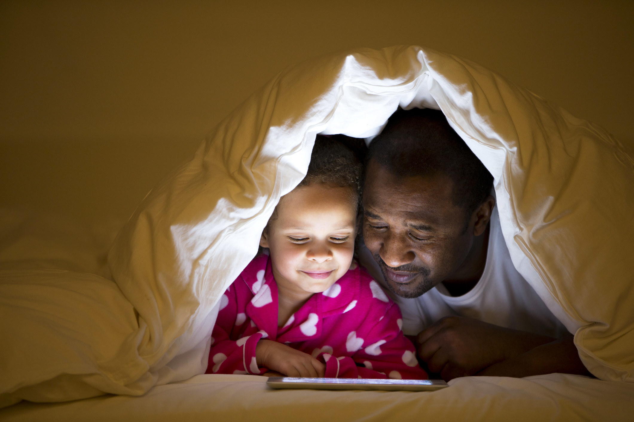 A father and son under the blankets using a tablet