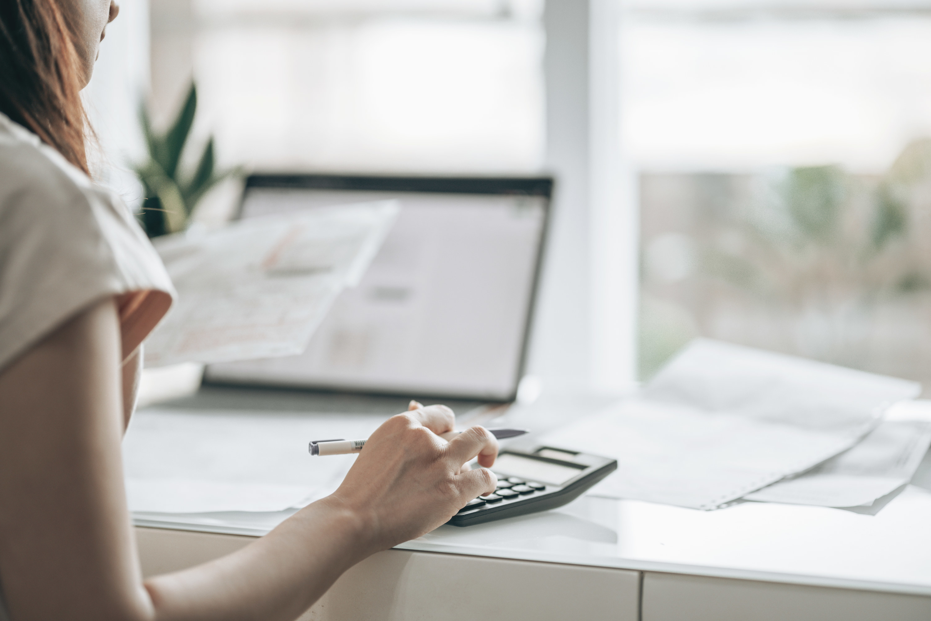 person typing in calculator on a white desk