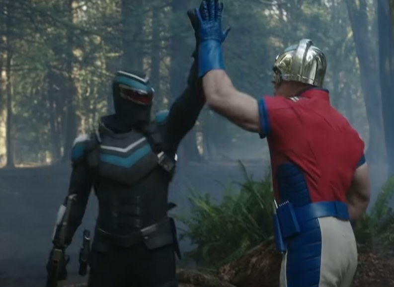 Vigilante played by Freddie Stroma and Peacemaker played by John Cena high fiving each other