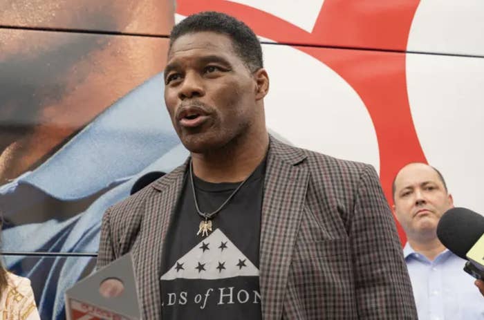 Herschel Walker stands at a press event with microphones pointing at him