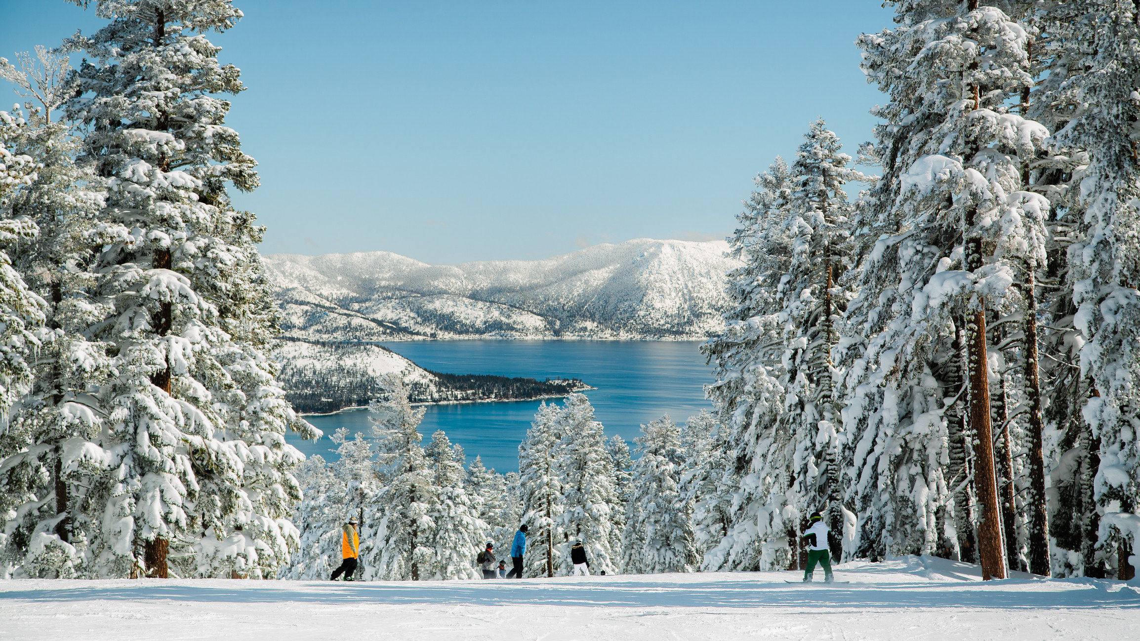 People skiing on top of a mountain with view of Lake Tahoe on a snowy winter day.