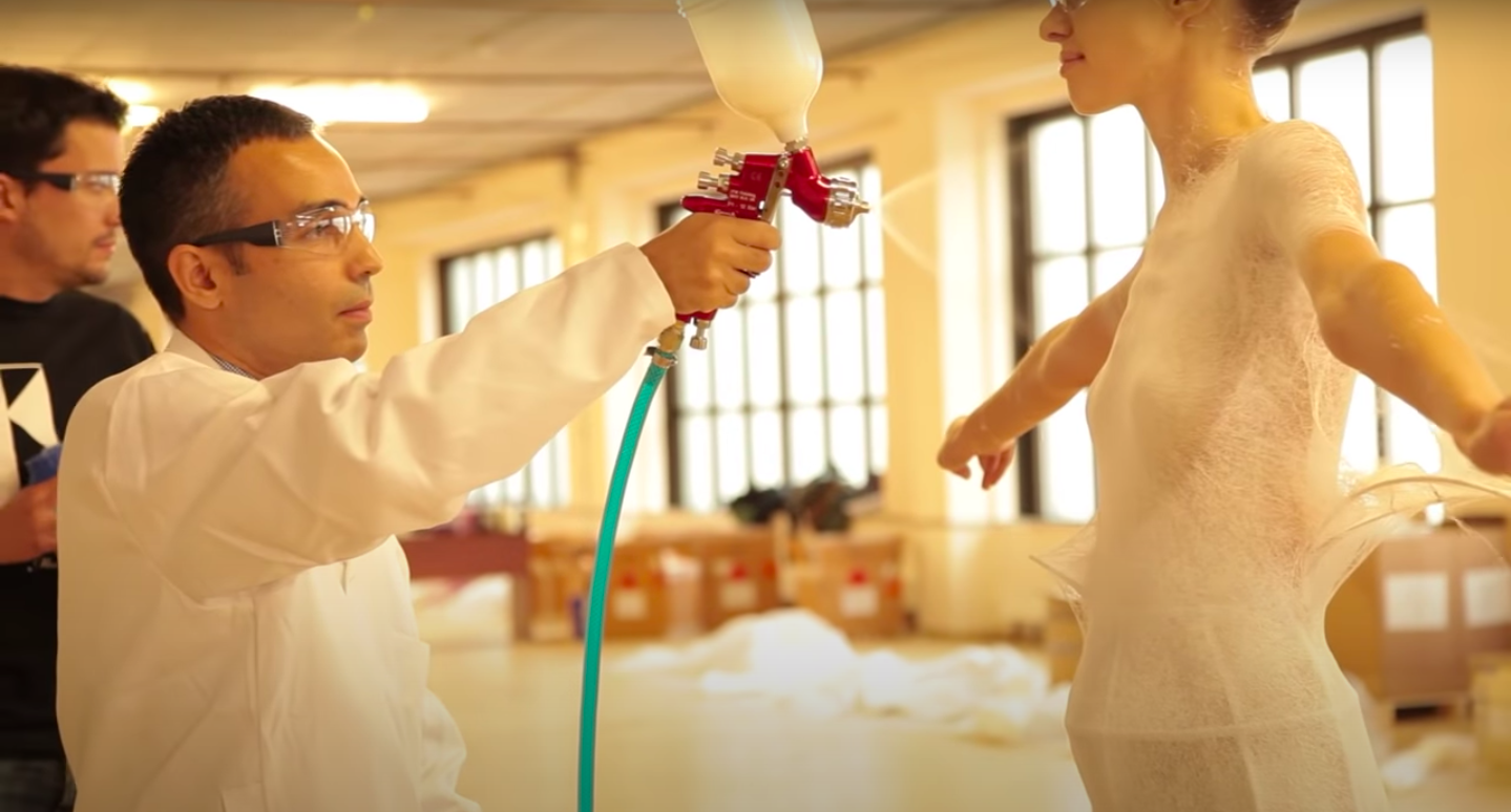 Man wearing goggles applying spray-on fabric to a model