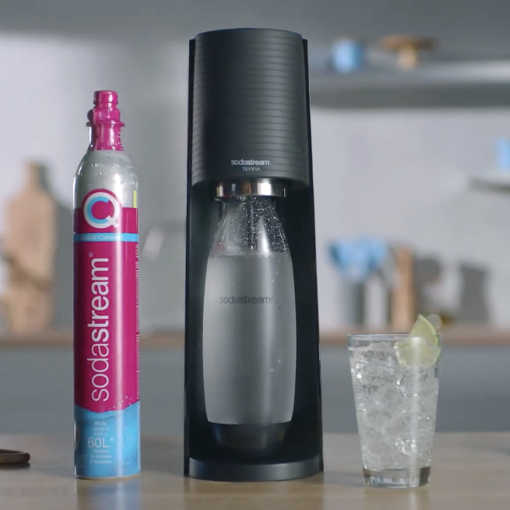 The black SodaStream with a glass of carbonated water next to it and a CO2 tank