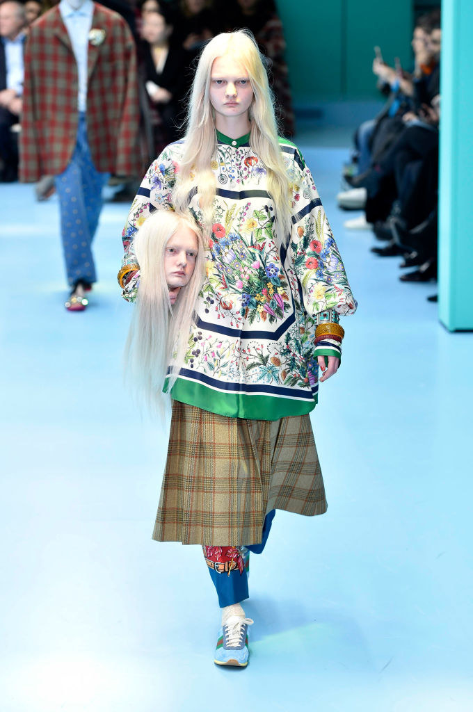 A model on the runway carrying a head that looks like them