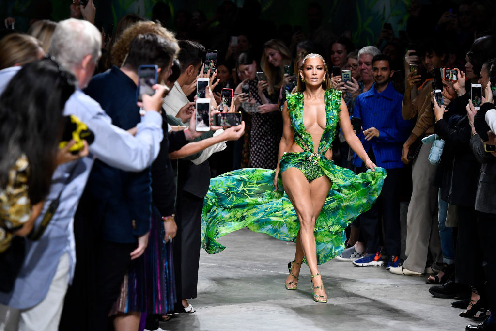 JLo walking the runway in a green, body-baring dress with an audience taking cellphone photos on either side