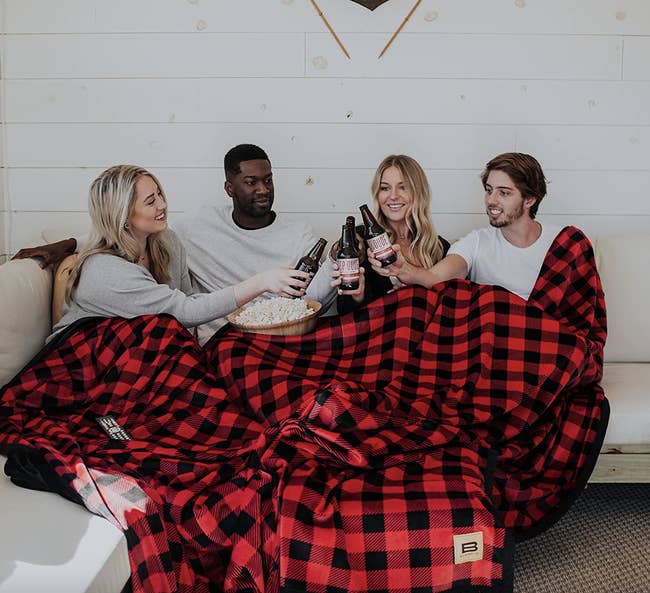 Four models inside a large red and black checkered blanket on the couch
