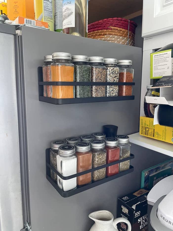 Reviewer image of two black magnetic racks filled with spices attached to the side of the fridge