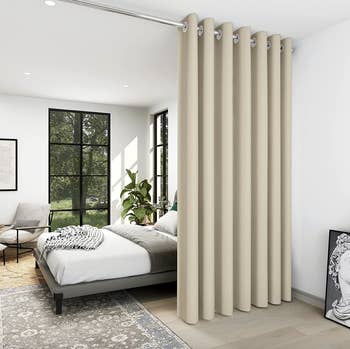 The beige blackout curtain hanging from the ceiling to separate two rooms