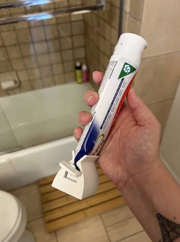 a BuzzFeeder using the white tube squeezer on a full tube of toothpaste