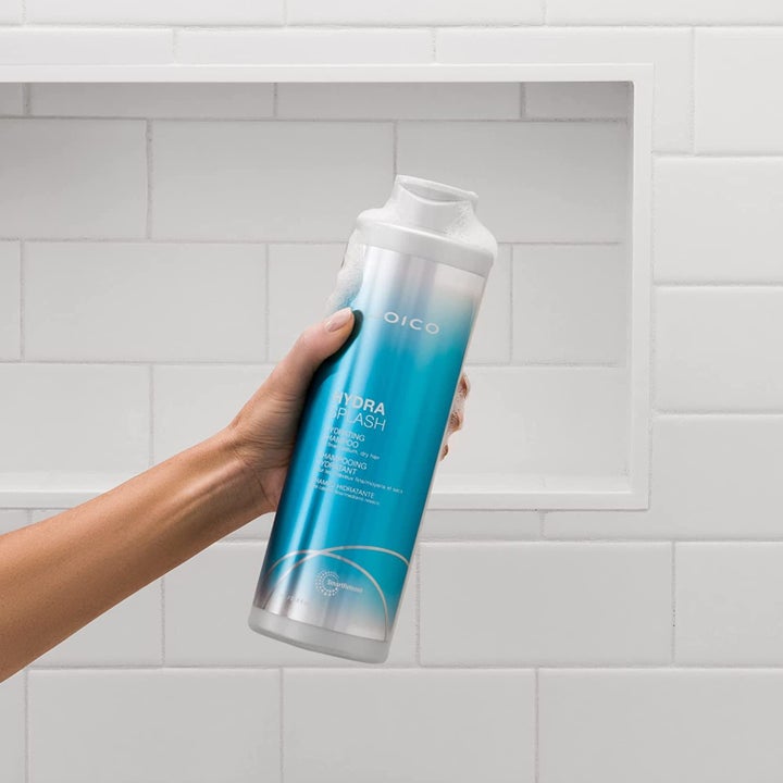 model holding the blue and white bottle of shampoo against a white tile background