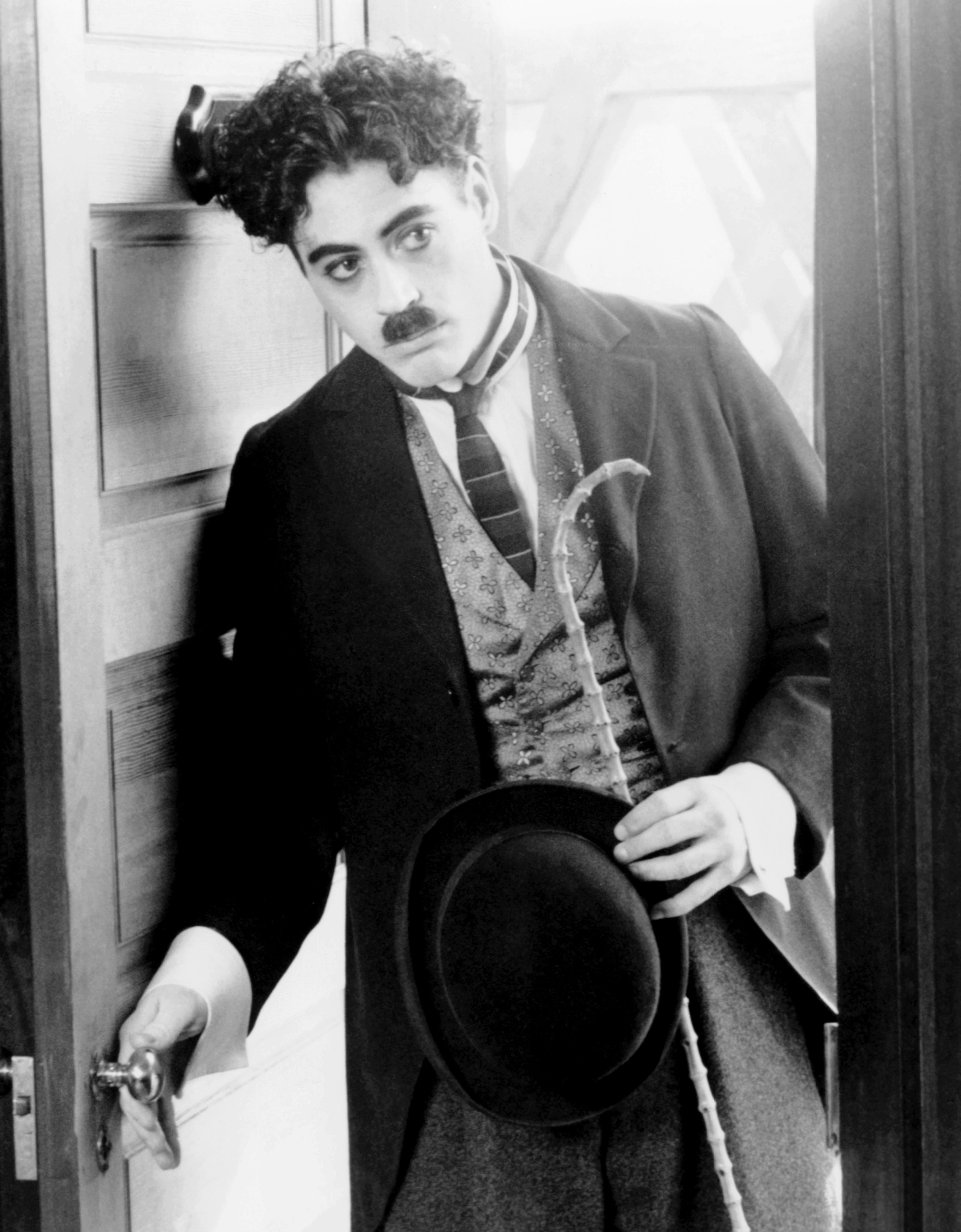 Robert in a black-and-white photo as Charlie with a small mustache and holding a hat