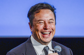 Elon Musk holding a microphone and smiling