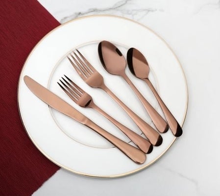 Rose gold knife, salad fork, dinner fork, tablespoon and teaspoon on white plate