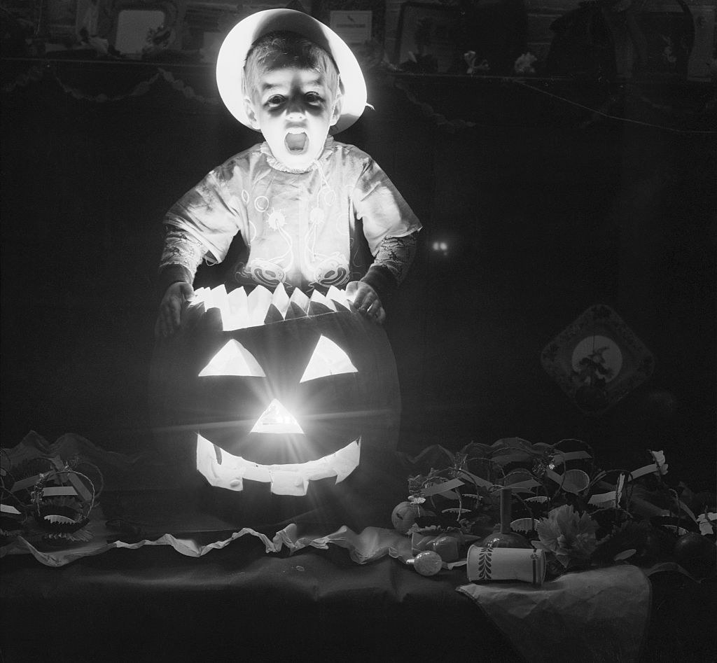 A child behind a lit-up Jack-o&#x27;-lantern