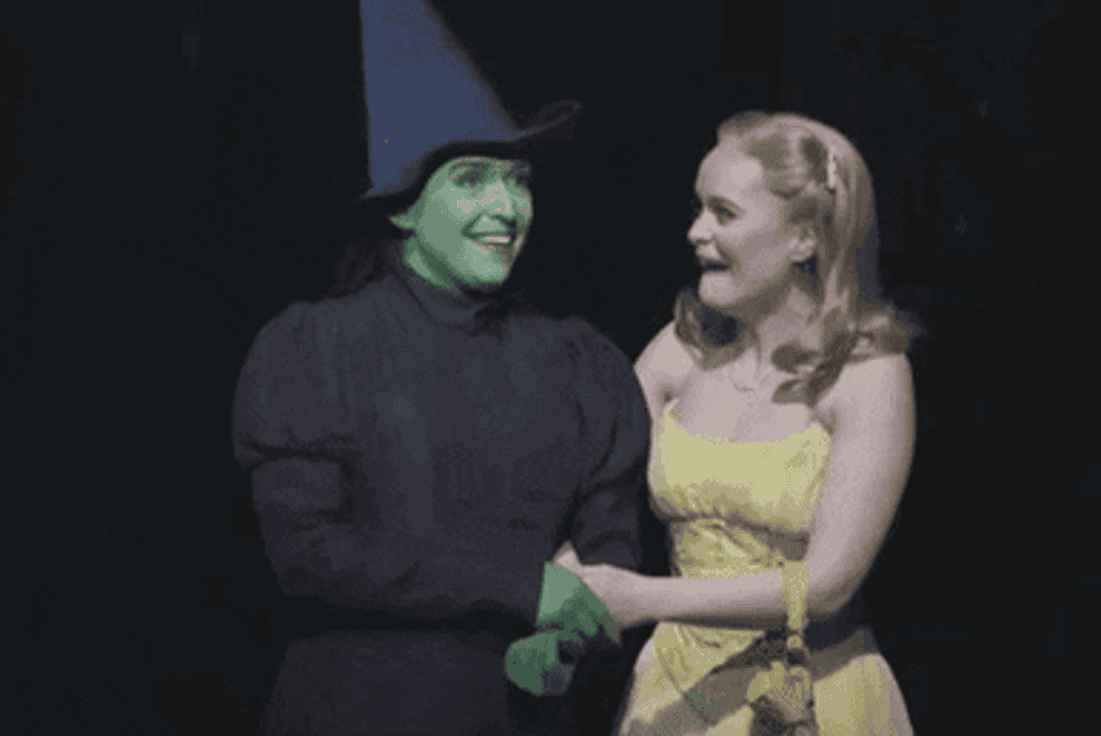 gif of actresses in wicked costumes holding each other and laughing