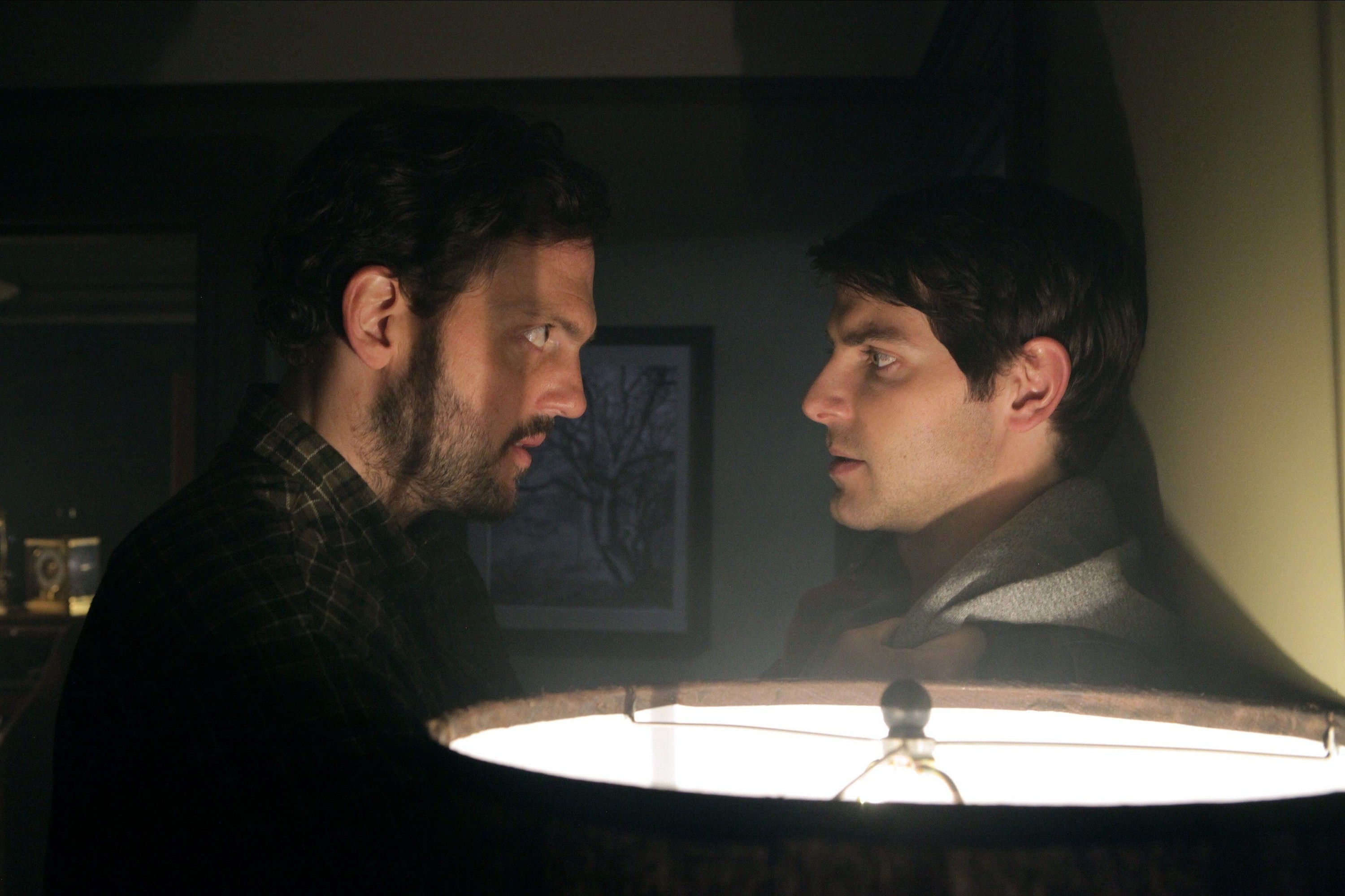 Two men have an intense nighttime staredown by a glowing lamp