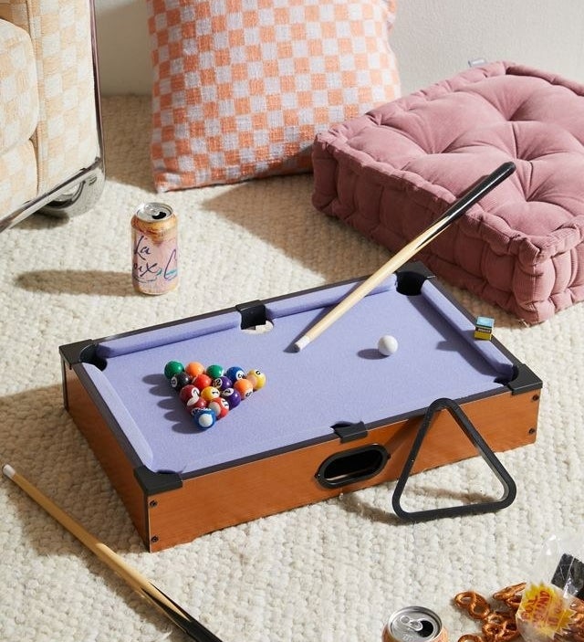 a mini pool table on a carpet surrounded by pillows