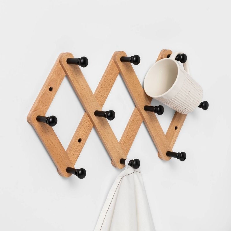 wood accordion wall hanging with 10 black hooks and a mug and towel hanging on two of them