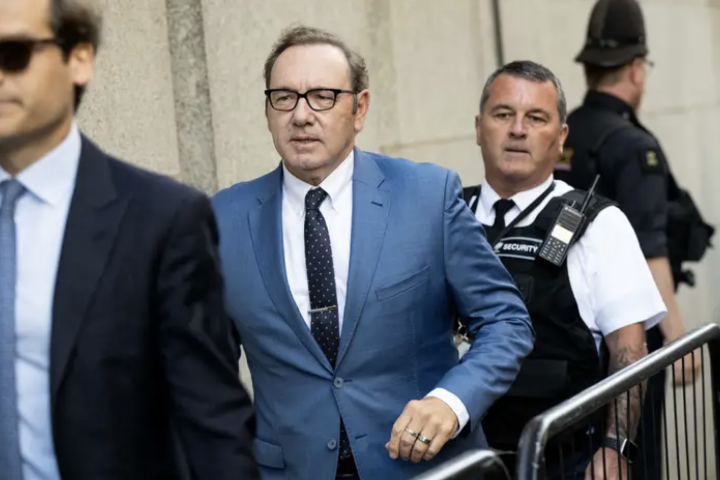 Kevin Spacey in a suit walking with security outside a courthouse