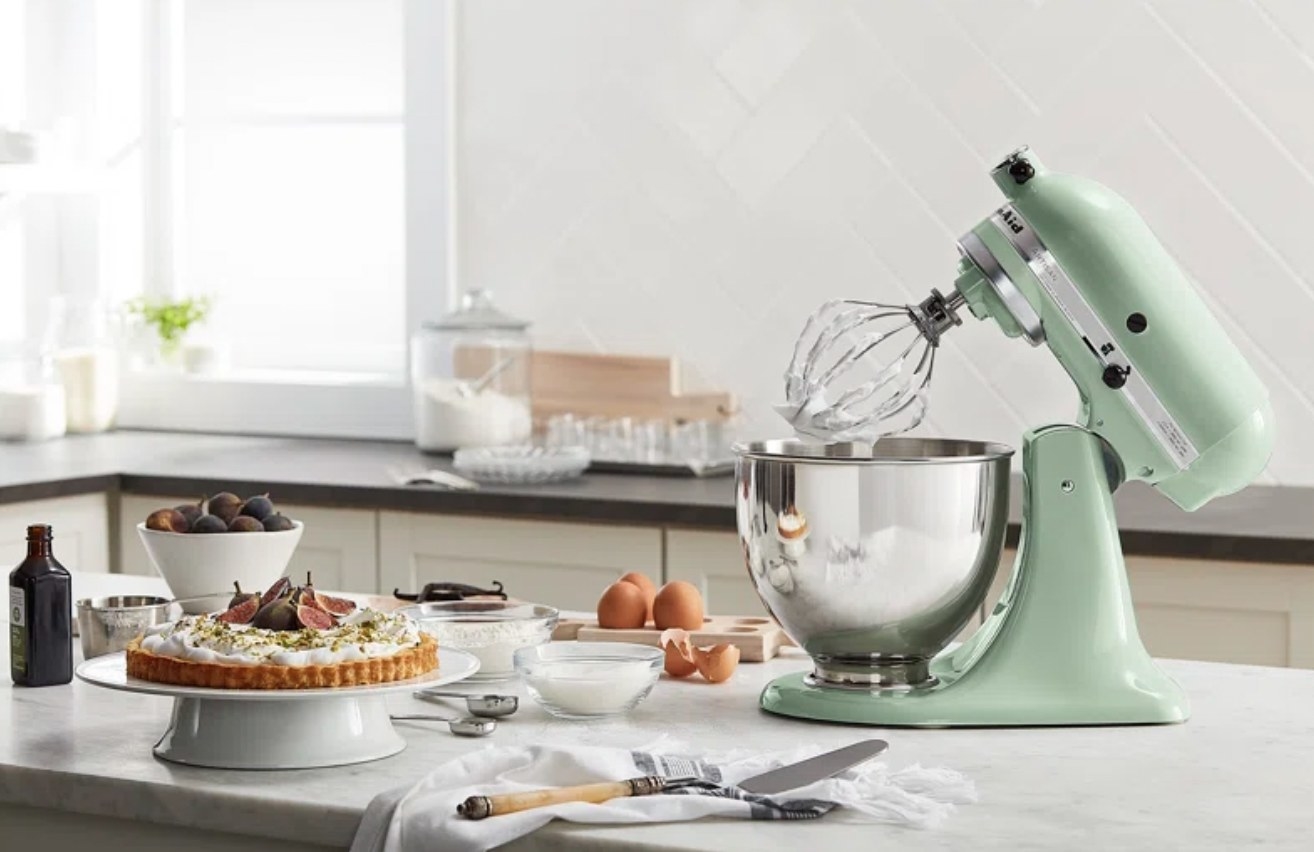 The mint mixer with top portion tilted back and whisking attachment coming out of metal bowl