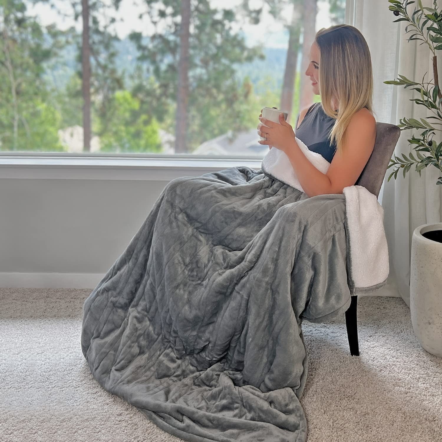 person sitting on a chair with a mug and the blanket on