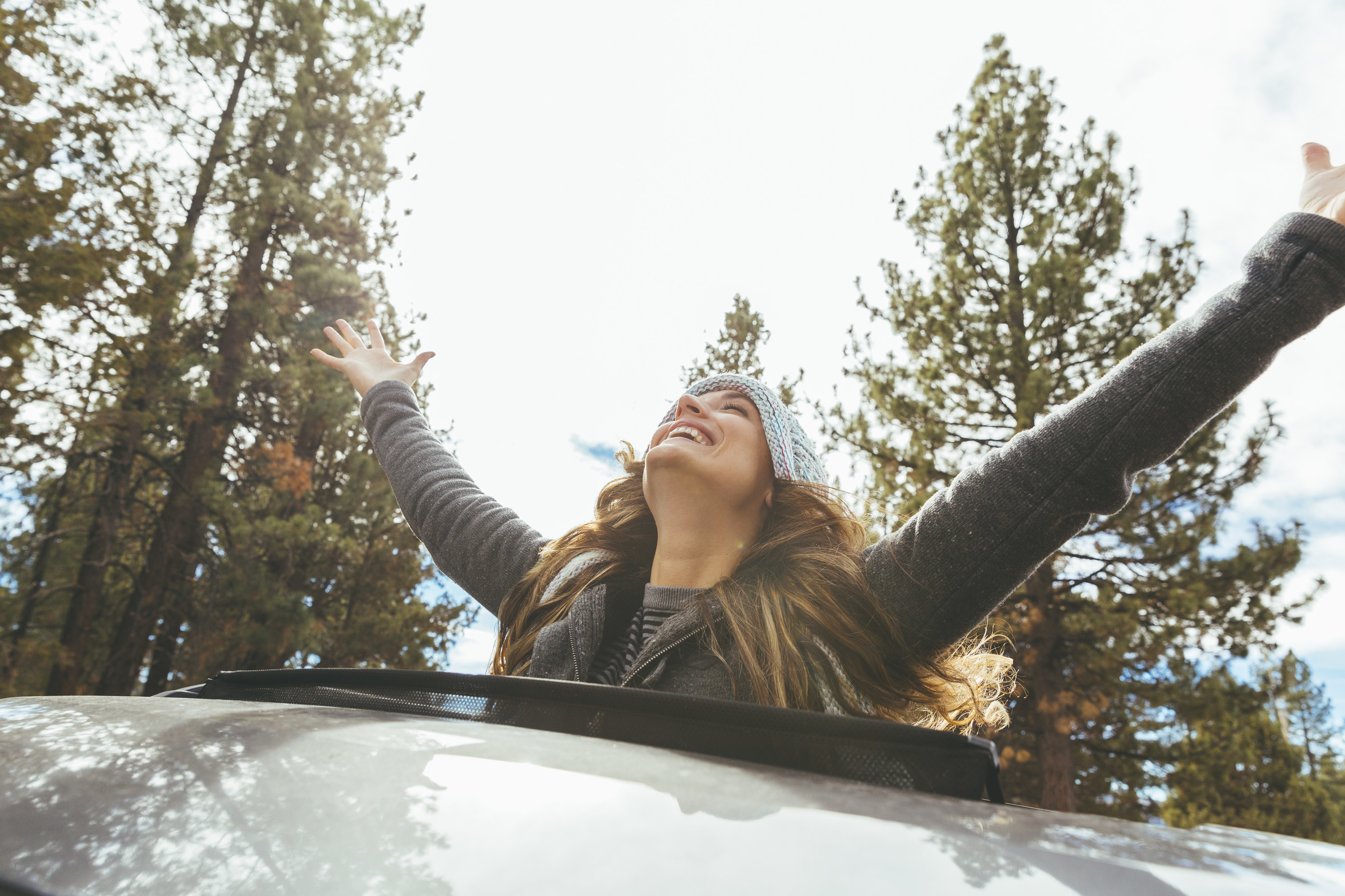 A woman smiles and raises her arms as she stands in a sunroof