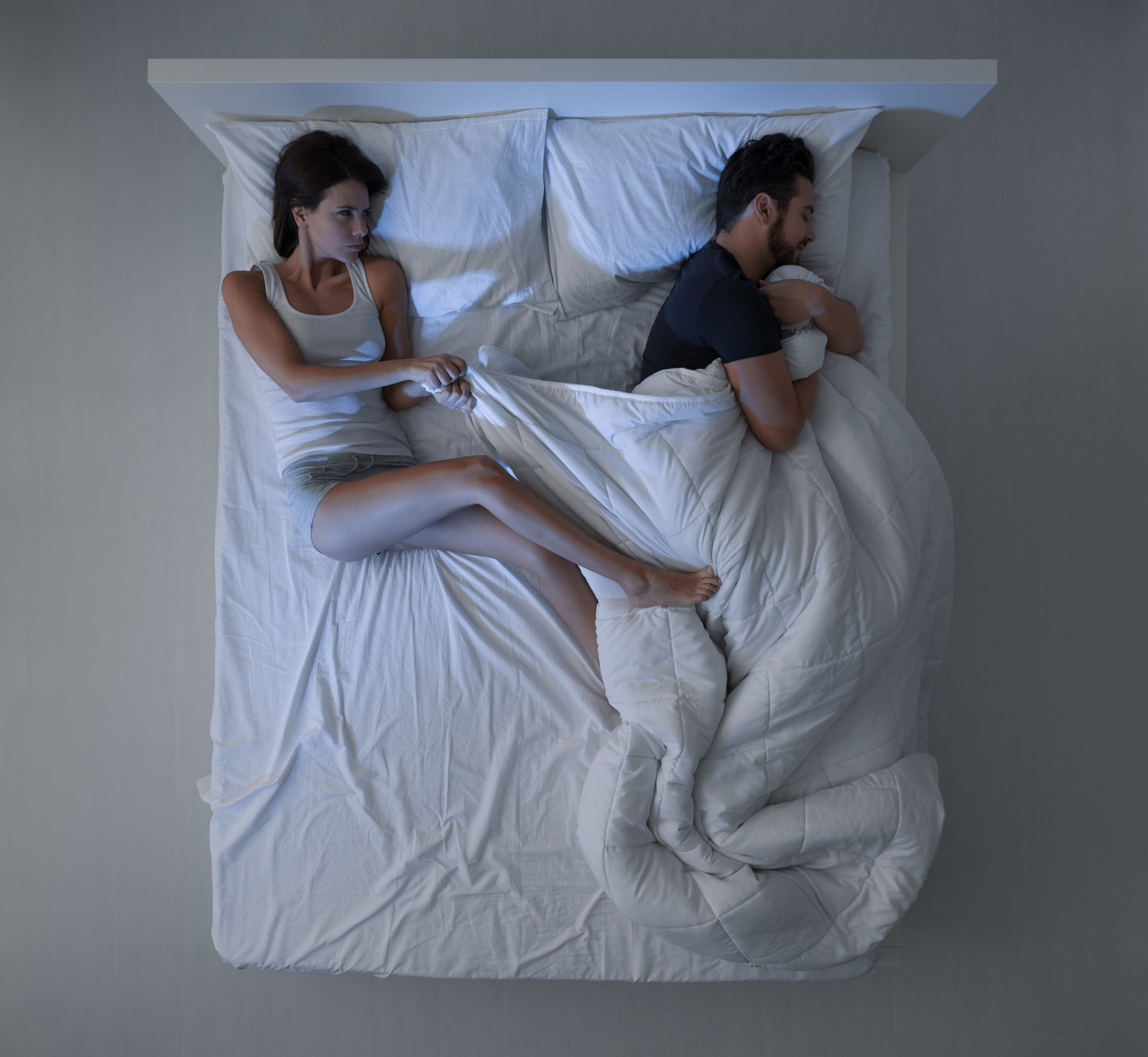 woman in bed trying to pull the covers from her partner