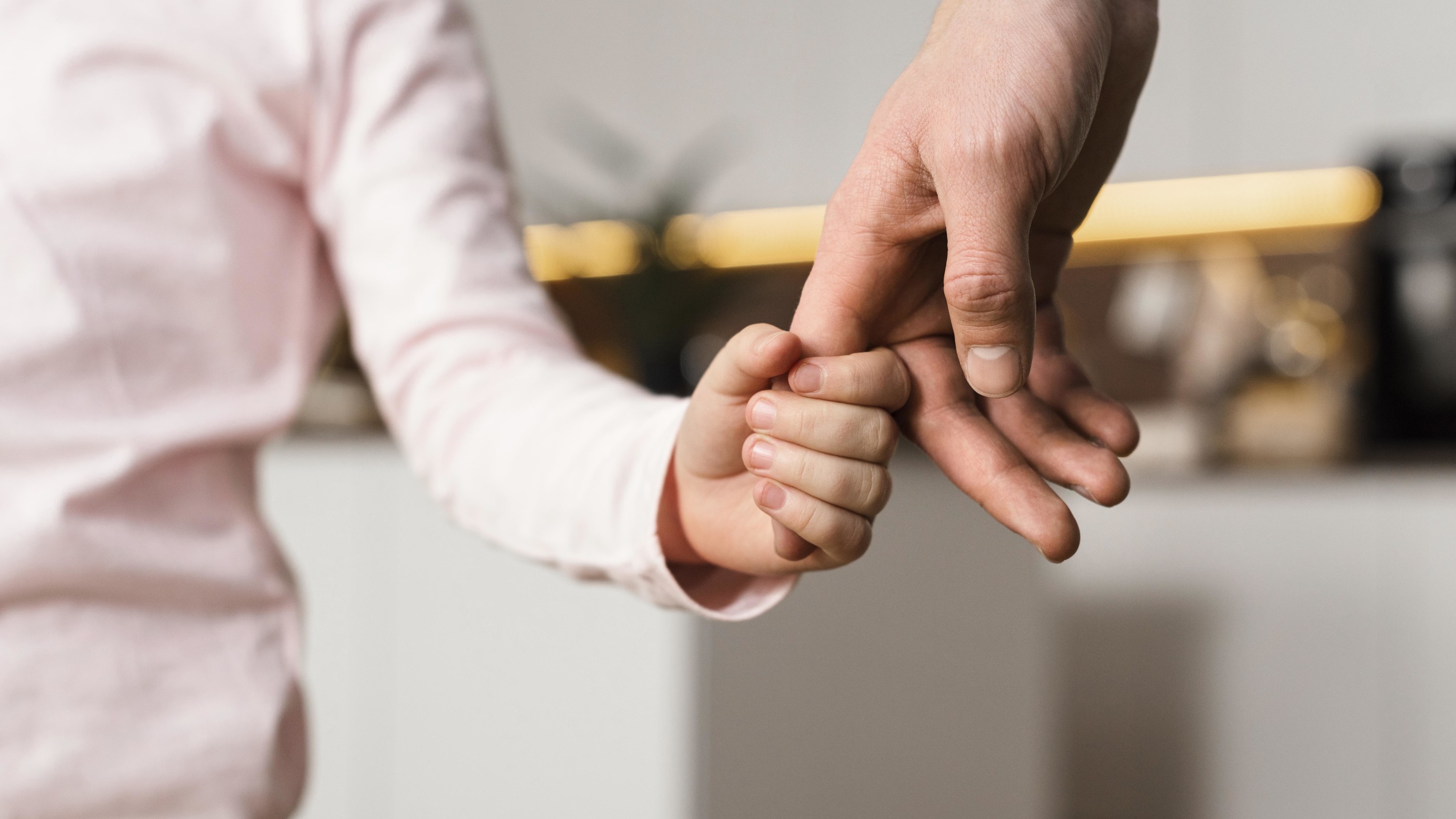 A young child holds the hand of their parent