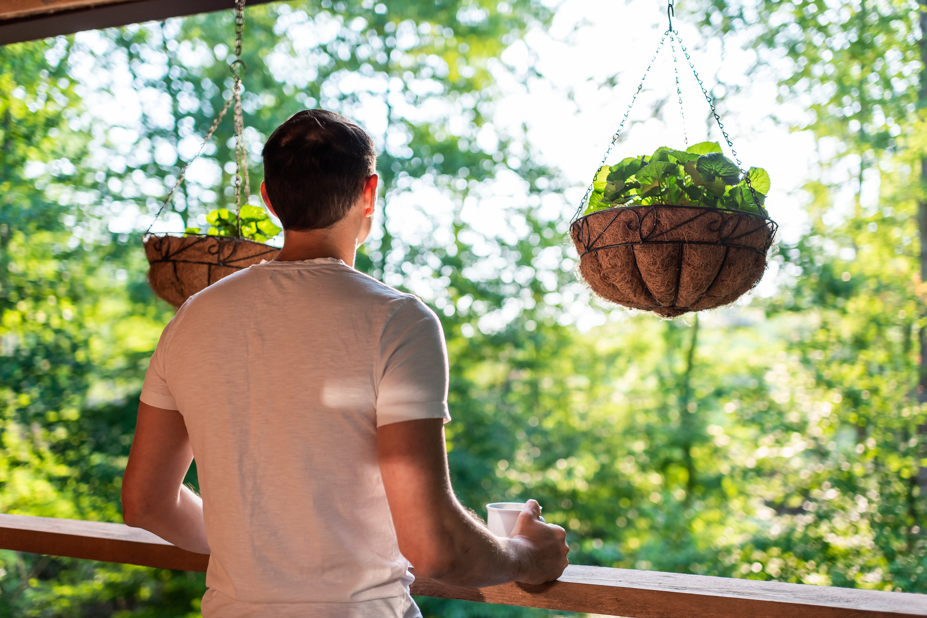 A man looks at the view of trees from his porch and drinks coffee