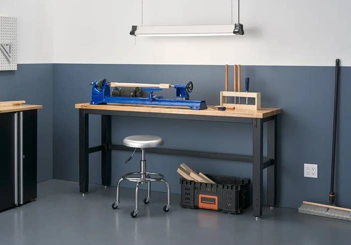 A wood and metal work bench with tools and a stool sitting next to it.