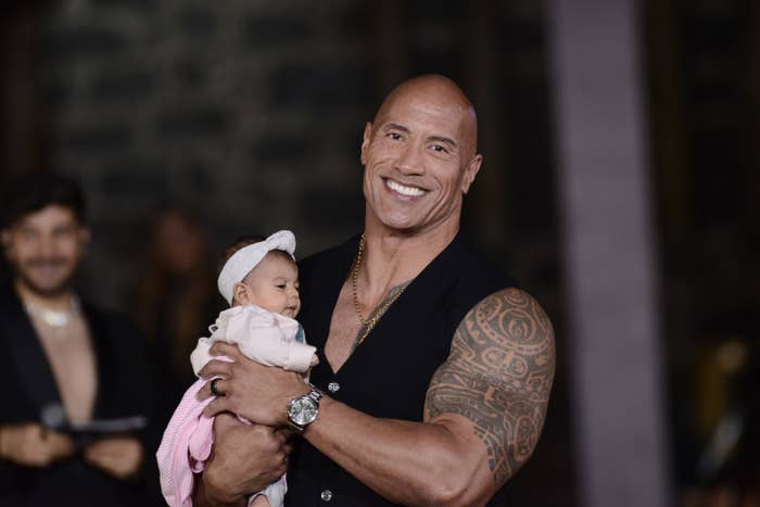The rock holding a baby and smiling