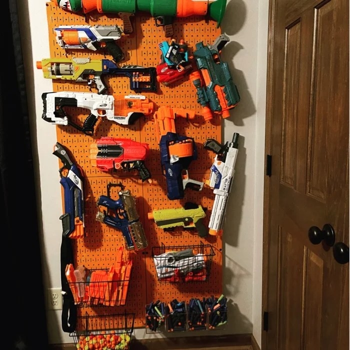 An orange peg board panel holding a variety of Nerf toys and storage baskets