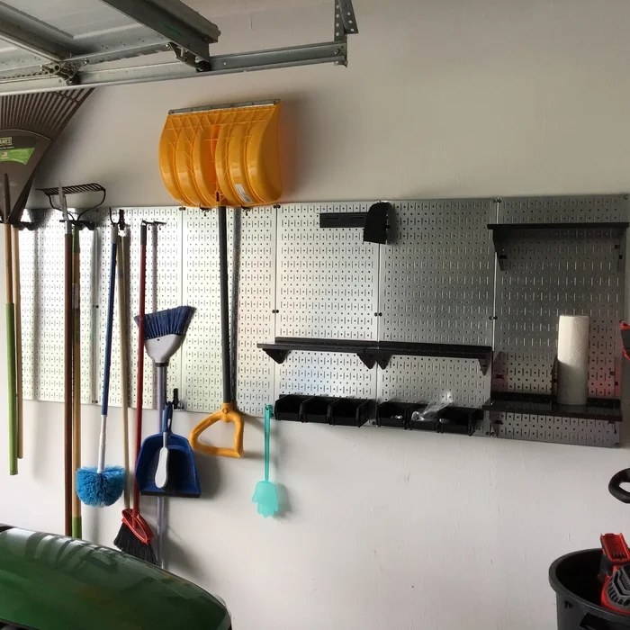 A galvanized and black pegboard with tools hanging on it