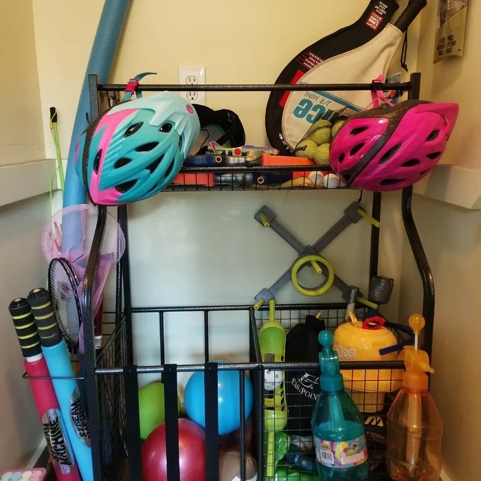 A black sports storage rack with a variety of equipment in the bins