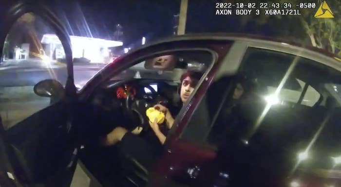 An image from police body camera footage shows Erik Cantu looking shocked as he eats a burger in the front seat of his car after the officer opened his car door