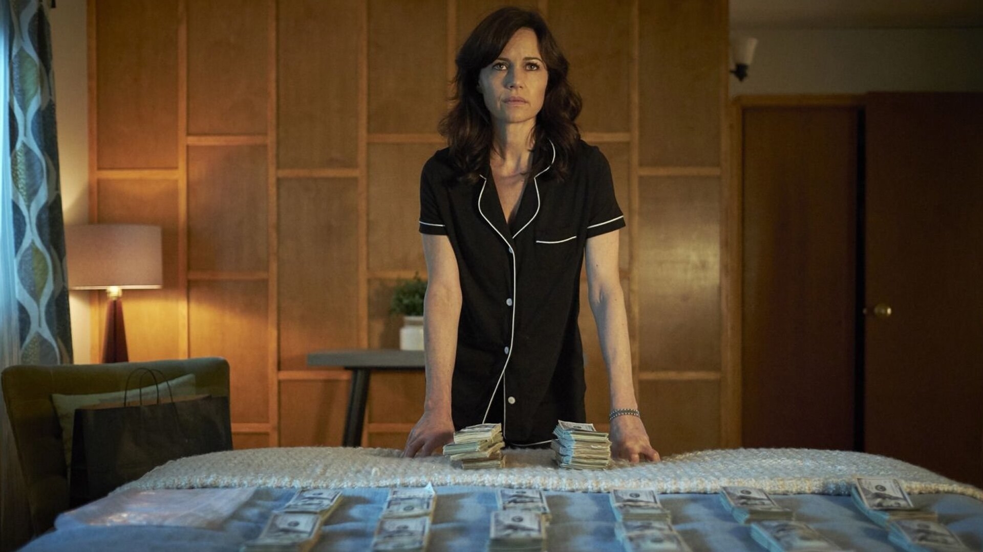 Carla Gugino stands over a bed of money